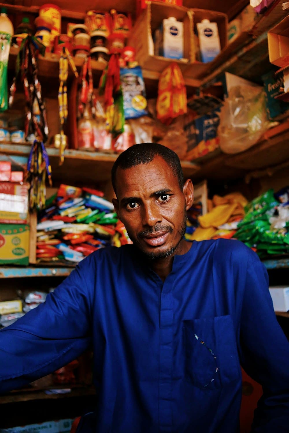 A shopkeeper standing behind the counter of a small, well-stocked shop.